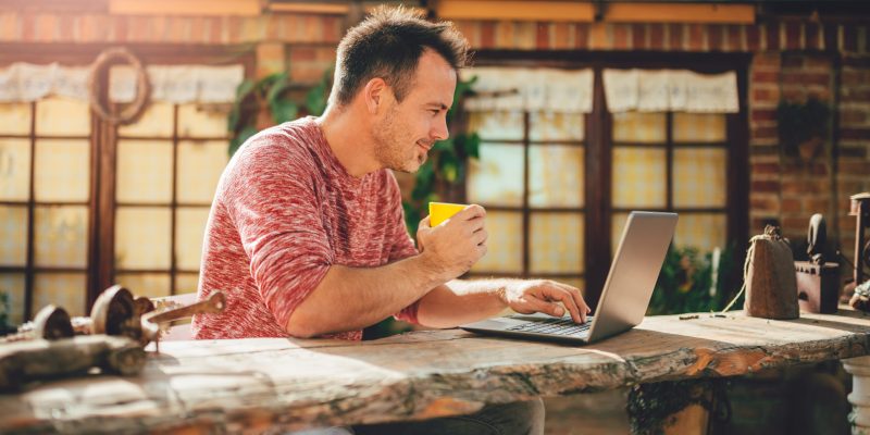 Men sitting in the at backyard patio drinking coffee and using laptop