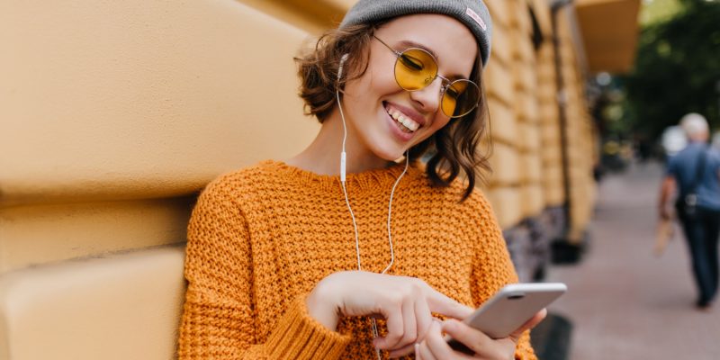 excited-young-woman-typing-message-standing-near-building-after-walk